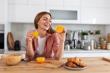 Beautiful young woman drinking fresh orange juice in kitchen. Healthy diet. Happy young woman with...