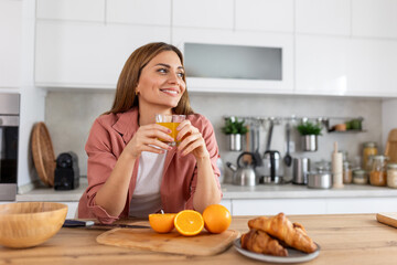 Beautiful young woman drinking fresh orange juice in kitchen. Healthy diet. Happy young woman with...