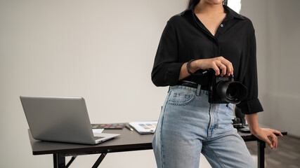 A cropped shot of a female photographer is standing in her studio with a DSLR camera in her hand.
