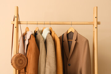 Rack of stylish clothes and handbag near beige wall