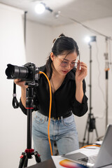 Cool, professional Asian female photographer is checking images on her laptop, working in the studio - obrazy, fototapety, plakaty