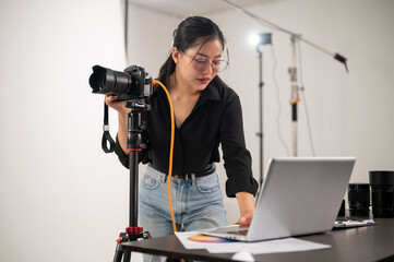 Cool, professional Asian female photographer is checking images on her laptop, working in the studio