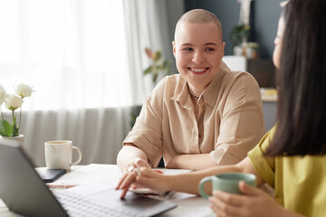 Selective focus shot of cheerful Caucasian woman with shaved head smiling while surfing Internet...