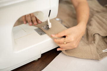 A close-up image of a female tailor is sewing a dress with a sewing machine, working in her studio.