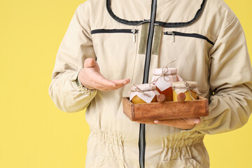 Male beekeeper with honey on yellow background, closeup