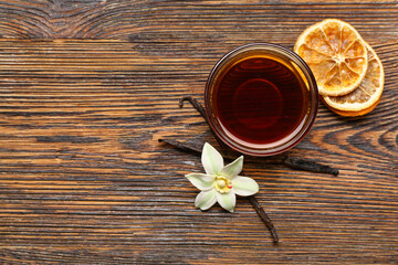 Bowl of vanilla extract, sticks and dried orange slices on wooden background