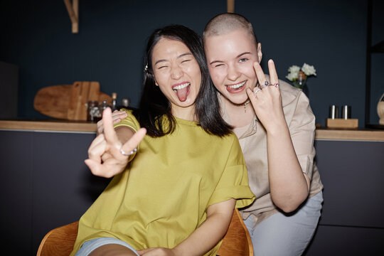Two ethnically diverse girl friends wearing casual clothes having fun posing for camera in kitchen, flash photo