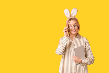 Happy adult businesswoman in bunny ears with tablet computer on yellow background. Easter celebration