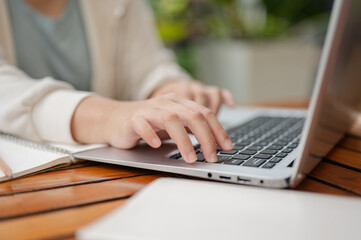 A cropped image of a woman is working remotely at an outdoor space, typing on laptop keyboard.
