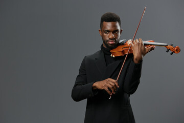 Elegant African American man playing violin in black suit on gray background for musical...