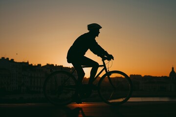 silhouette of a cyclist during a city sunset - obrazy, fototapety, plakaty