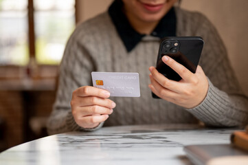 An Asian woman holding her smartphone and a credit card, sitting at a table indoors
