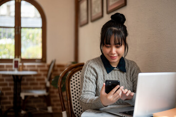 A woman is checking messages on her smartphone while working remotely at a coffee shop.
