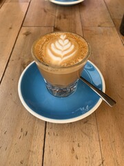 A cortado coffee served in a glass on a blue saucer against a wooden background