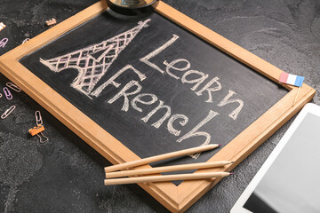 Chalkboard with text LEARN FRENCH, stationery and tablet computer on dark background, closeup