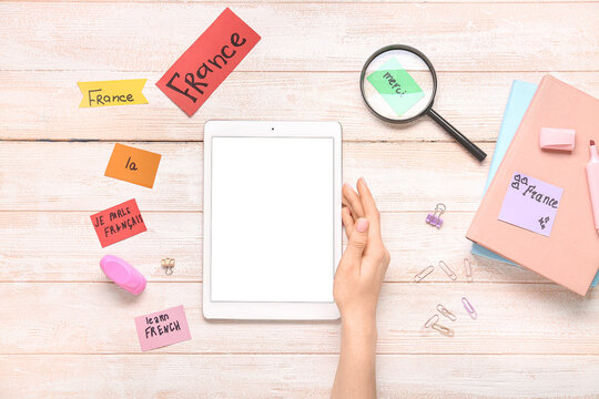 Female hand with modern tablet computer, stationery and French words on white wooden background