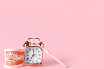 Alarm clock, model of jaw with dental braces and toothbrush on pink background
