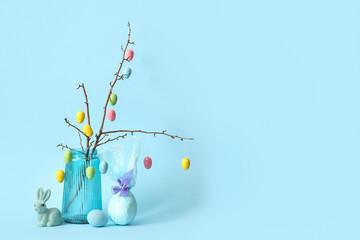 Branches with Easter eggs in glass vase, rabbit and gift egg on blue background