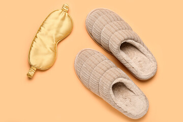Pair of beige soft slippers and sleep mask on beige background. Top view