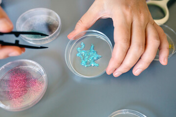 Close up of female scientist hand holding a blue glitter sample over petri dish on a environment research laboratory. Woman chemist technician analyzing dangers of microplastics composition.