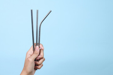 Hand holding reusable stainless steel straws on blue background. Eco friendly concept.