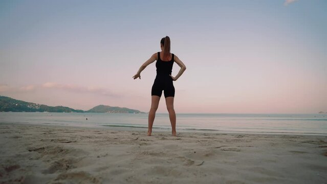 Barefooted woman doing yoga exercise lounge, warrior pose on sandy sea ocean beach at sunset. Female stretching legs. Body care, wellness, healthy lifestyle, morning sport female training concept.