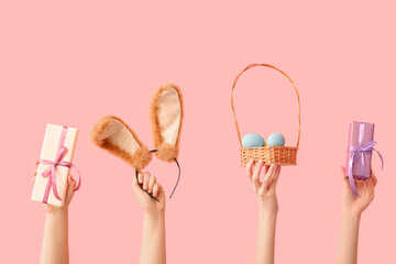 Female hands with bunny ears headband, gifts and Easter eggs wicker basket on pink background