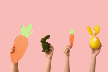 Female hands with Easter bunny, gift egg and paper carrots on pink background