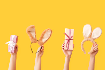 Female hands with gifts and Easter bunny ears headbands on yellow background