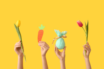 Female hands with gift egg, paper carrot and tulips on yellow background. Easter concept.