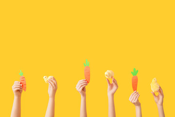 Female hands with chicks and paper carrots on yellow background. Easter concept.