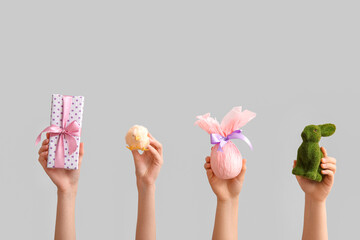 Female hands with Easter bunny, chick and gift egg on grey background