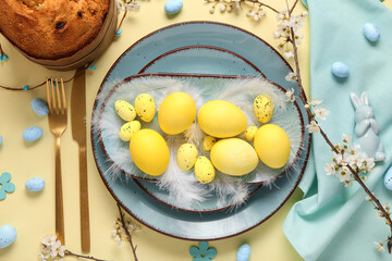 Beautiful table setting with Easter eggs and Easter cake on yellow background