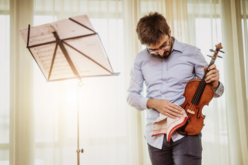 Man playing violin at home. He is cleaning his instrument.