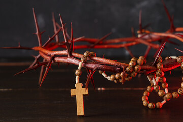 Crown of thorns and beads with cross on wooden table against black grunge background, closeup. Good...