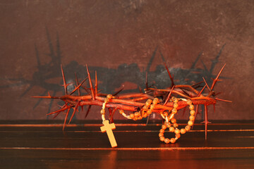 Crown of thorns and beads with cross on wooden table against black grunge background. Good Friday concept
