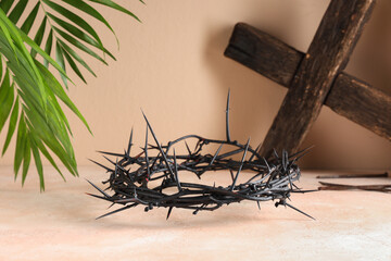 Crown of thorns with wooden cross and palm leaves on beige background. Good Friday concept