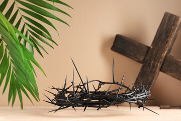 Crown of thorns with wooden cross and palm leaves on beige background. Good Friday concept