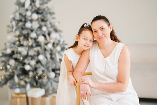 Gentle mother and daughter in white dresses at the Christmas tree. Happy family. Love and care.