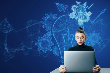 Attractive thoughtful young businesswoman using laptop at desk with glowing blue lightbulb,...