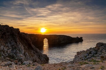 view of the landmark stone arch of Pont d'en Gil on Menorca Island at sunset