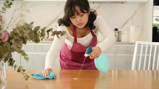 Young housewife cleaning table surface with rag in modern kitchen