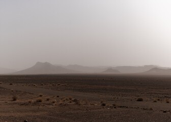 desert landscape with arid hlls in the distance under a hazy sandstorm sky in southern Morocco