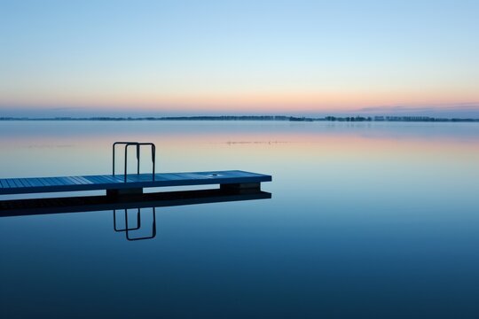 empty diving board over calm water at sunrise