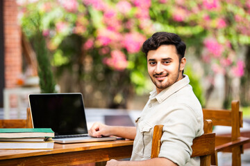 Indian handsome student or businessman using laptop computer outdoors while sitting on table