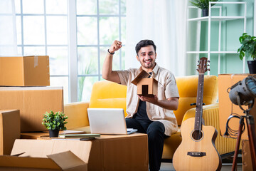 Home moving concept showing indian young man using laptop or smartphone while surrounded with...