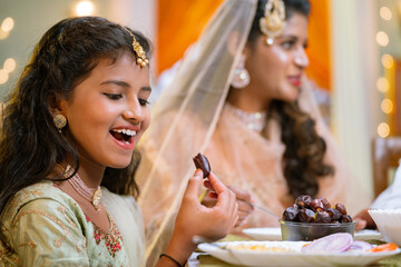 Happy excited indian girl eating dates while having dinner during Ramadan iftar or dinner with family - concept of healthy eating, ramzan iftar and relationship