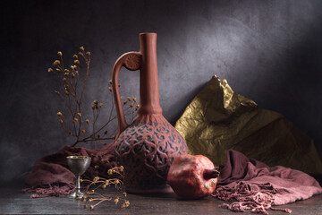 Still life with a clay jug and pomegranate on a dark background