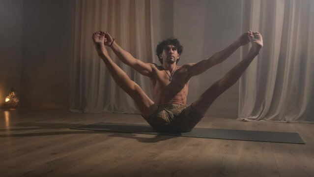 A young man is engaged in yoga exercises spreading his legs apart.