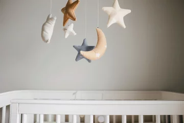 Poster star and moon mobile spinning above a white crib © studioworkstock